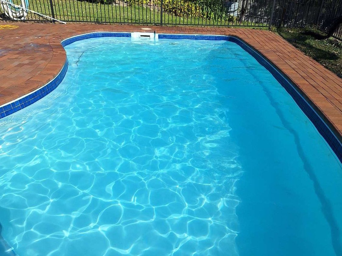 The same swimming pool after treatment, water clear and blue with the pool floor visible